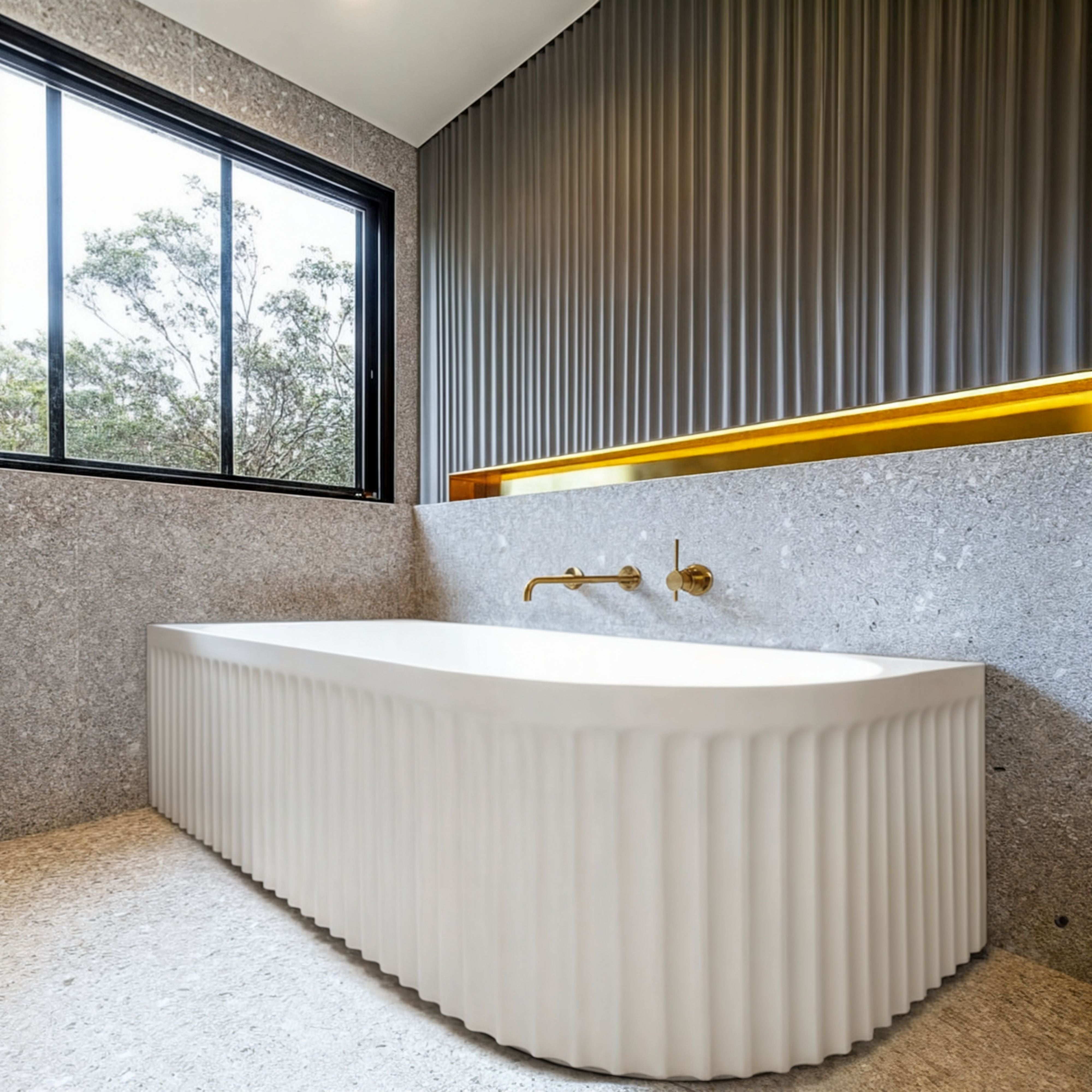 Fluted matte white corner bathtub against terrazzo walls with brushed brass tapware and timber accents.